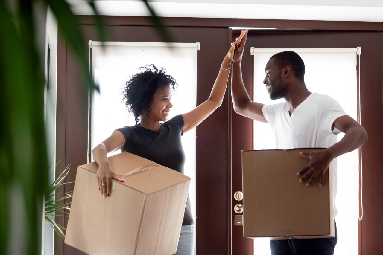A couple celebrates with a high-five in the doorway of their new home, moving boxes stacked beside them.